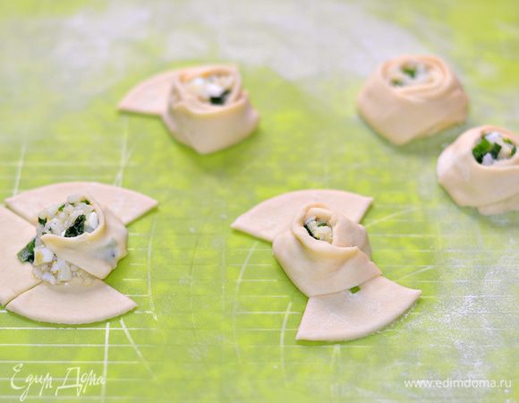 Часть теста раскатать в пласт толщиной примерно 4 мм. Стаканом (большим в диаметре) вырезать заготовки. Сделать крестообразно надрезы, примерно по 3 см с каждой стороны, получается 4 сегмента. В центр каждой заготовки выложить начинку — примерно 2 ч. л.. Первым сегментом как бы оборачиваем начинку, далее 2-й сегмент и т. д., как показано на фото.