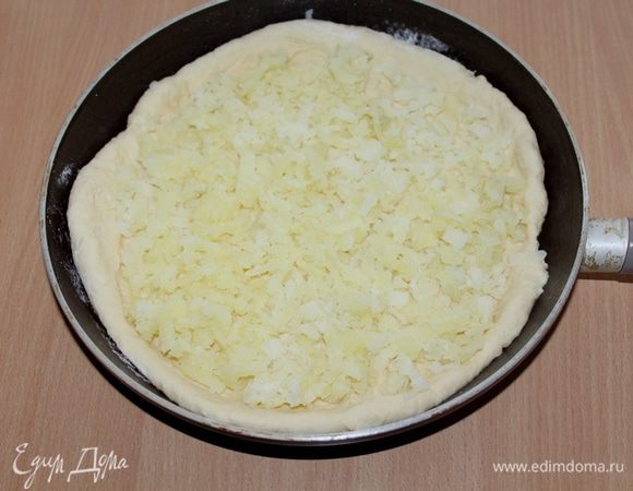 Отделяем 2/3 теста и выкладываем в сковороду, руками распределяя тесто, формируя небольшие бортики.
Выкладываем натертый картофель.