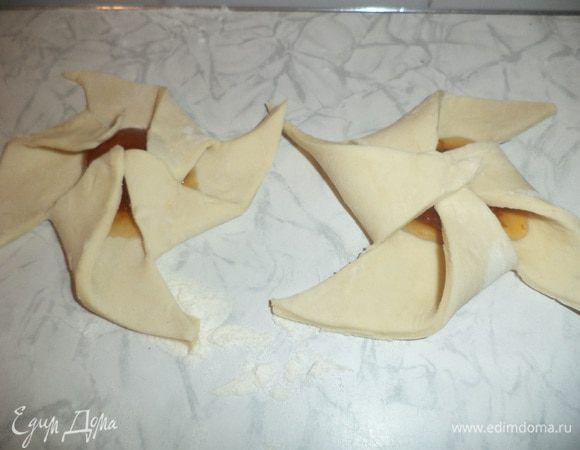 Противень смазать маслом, выложить на противень слойки, два уголка слегка отогнуть, в серединку положить половинку абрикосы из варенья, накрыть отогнутыми уголками.