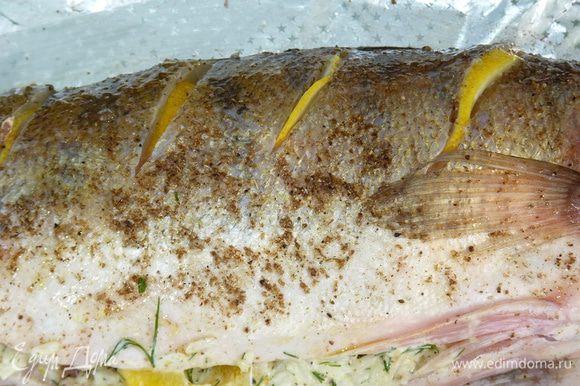 По спинке рыбы с двух сторон сделать глубокие надрезы, посолить внутри. Лимон нарезать полукольцами и вставить в «кармашке».