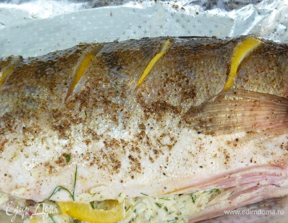 По спинке рыбы с двух сторон сделать глубокие надрезы, посолить внутри. Лимон нарезать полукольцами и вставить в «кармашке».