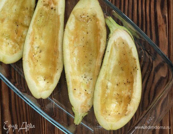 Духовку разогреваем до 200°С. Баклажаны моем, разрезаем пополам вдоль. Большой ложкой аккуратно выскабливаем мякоть, не повреждая кожицу. Мякоть оставляем. Выкладываем лодочки из баклажанов в форму для запекания, солим, перчим и немного смазываем оливковым маслом, чтобы они не подсохли в духовке. Запекаем 10–15 минут.