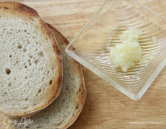 Хлеб (у меня домашний) поджарить в тостере или на гриле. Чеснок выдавить с помощью пресса и смешать с оливковым маслом. Намазать каждый кусок хлеба с обеих сторон чесночным маслом.