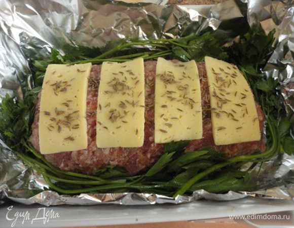 Закрыть начинку фаршем и сформовать рулет. Сверху выложить ломтики сыра, посыпать тмином, по бокам положить зелень, накрыть фольгой.