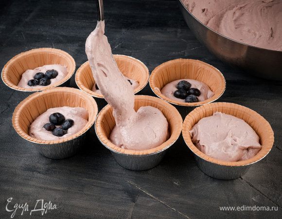 В формы для маффинов вставить бумажные вкладыши, выложить понемногу теста, поместить в центр чернику, сверху добавить еще теста.
