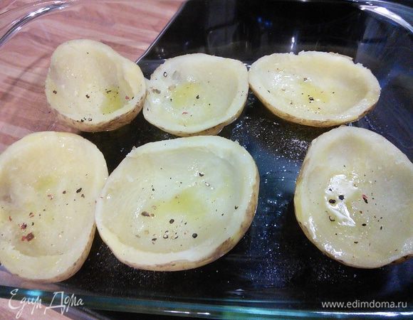 Крупный картофель можно отварить заранее до готовности. Остудить. Разрезать вдоль пополам. Чайной ложкой выберите серединку, оставив бортики. Большую форму для запекания смазать маслом, выложить картофель, посолить и поперчить, сбрызнуть оливковым маслом. Духовку разогреть до 175°С .