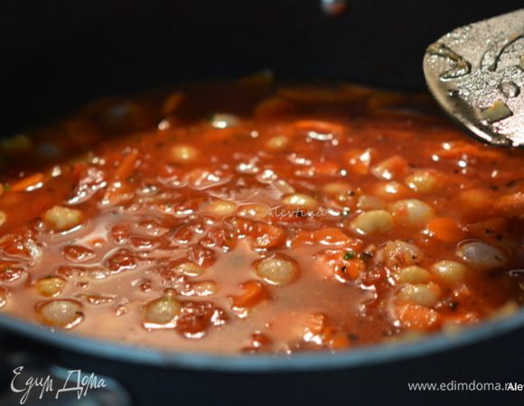 В блюдо с частью лука добавить паприку, морковь колечками примерно 1 стакан, готовить 1 минуту. Добавить томаты баночные острые или с добавлением остроты, промытый баночный  готовый нут, куриный бульон. Готовим помешивая 6 минут примерно.
