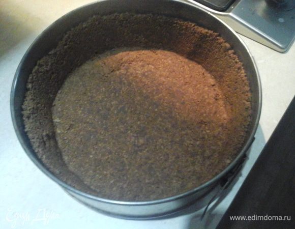 Сначала готовится основа: масло сливочное должно быть очень мягким, поэтому достаем его предварительно. Печенье измельчаем в крошку, добавляем сливочное масло и вымешиваем влажное рассыпчатое тесто. В форму на дно укладываем пергамент. Высыпаем тесто и приминаем его плотно ко дну и стенкам.