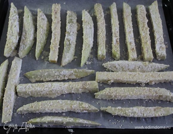 Баклажаны сперва обмануть с яично-сметанную смесь, затем обвалять в муке и кунжуте. Выложить на противень, покрытый бумагой для выпечки. Выпекать 15-20 минут при 180°С до золотистой корочки.