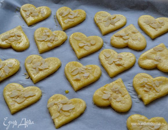 Выложить печенье на застеленный пекарской бумагой противень на небольшом расстоянии друг от друга (печенье в процессе выпечки увеличится в размере), смазать взбитым яйцом и посыпать миндальными лепестками.