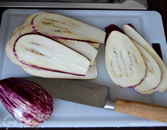 Баклажаны вымыть и нарезать тонкими ломтиками вдоль. Пересыпать солью и оставлять на время не нужно (но если вам так привычнее, то можете проделать эту процедуру).