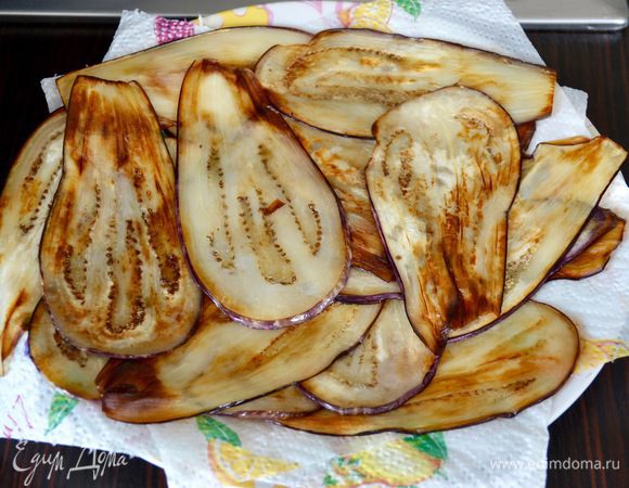 Обжарить баклажаны в небольшом количестве растительного масла до золотистого цвета. Готовые ломтики выкладывать на бумажное полотенце (или специальную бумагу для фритюра), чтобы они отдали лишний жир.