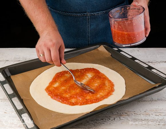 Когда тесто готово, раскатываем его тонким слоем и кладем на противень, покрытый бумагой для выпечки (бумагу для выпечки слегка смазываем оливковым маслом). Смазываем тесто слоем соуса.