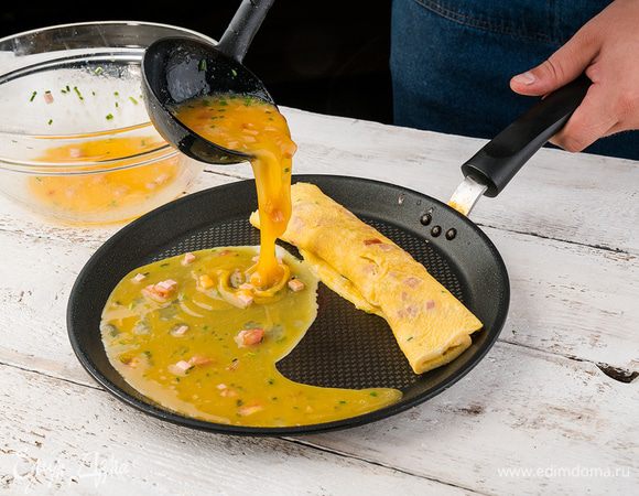 В тяжелой сковороде разогреть 1 ст. ложку оливкового масла и тонким слоем влить половину яичной смеси. Как только яичный корж схватится, немного завернуть один его край наверх, сдвинуть омлет на освободившееся место и половником влить еще немного яичной массы.
