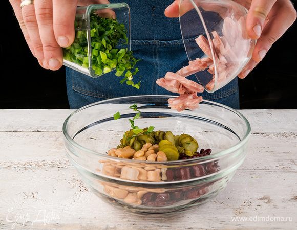 Из фасоли слить рассол, выложить ее в большую миску. Колбасу и огурцы нарезать соломкой. Зелень вымыть, обсушить. Зеленый лук нарезать колечками, с петрушки снять листики. Петрушку можно заменить на кинзу. Добавить к фасоли колбасу, огурцы и зелень, перемешать.
