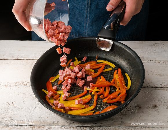 Перцы нарезаем полосками и обжариваем на среднем огне минут 10 до мягкости. В середине приготовления (через 5 минут) добавляем кубики колбасы.