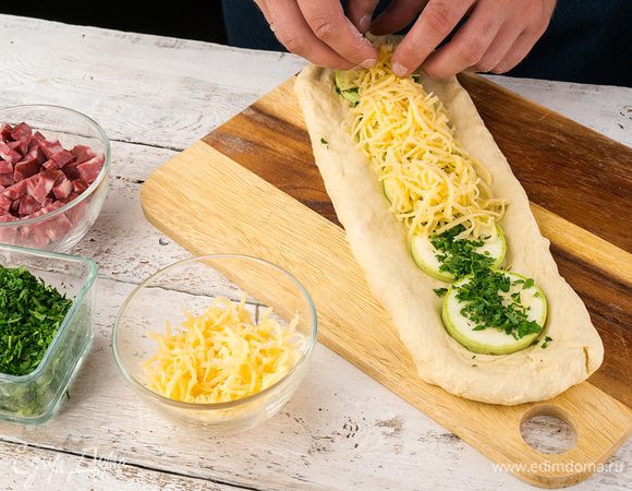 Выложить половину теста, выложить на него кабачок, нарезанный кружочками, посолить, на него высыпать потертый сыр, смешанный с зеленью и чесноком, поперчить. 