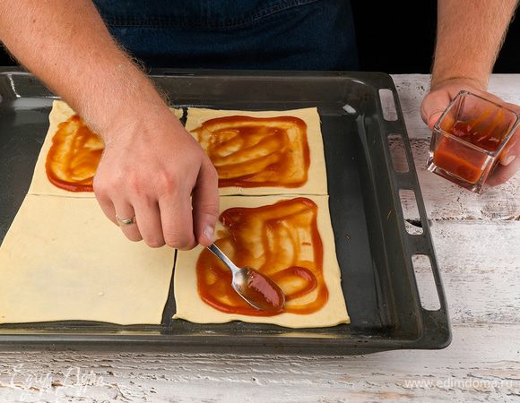 На рабочую поверхность слегка выложим муки, тесто и обминаем примерно 5 мин. Тесто должно быть эластичным и мягким. Раскатываем тесто, затем разрезаем на квадраты, должно выйти 6 квадратов. Каждый квадрат смазываем кетчупом или томатным соусом по центру, не задевая кончики краев.
