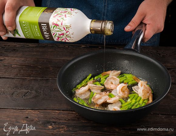 Разогреть в сковороде кунжутное масло и обжарить размороженные креветки почти до готовности, затем добавить спаржу и обжаривать все еще 3 — 4 минуты. Зеленый лук тонко порезать наискосок.
