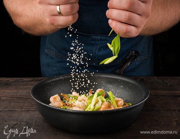 К креветкам со спаржей добавить кунжутное семя, зеленый лук, все перемешать, влить заправку, снова перемешать и прогревать еще около минуты.