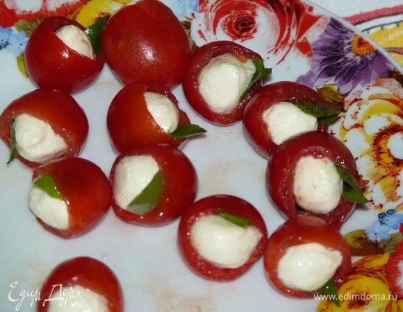 Оторвать листики базилика.  Шарики моцареллы разрезать пополам и вставить в помидоры вместе с листочками базилика.
