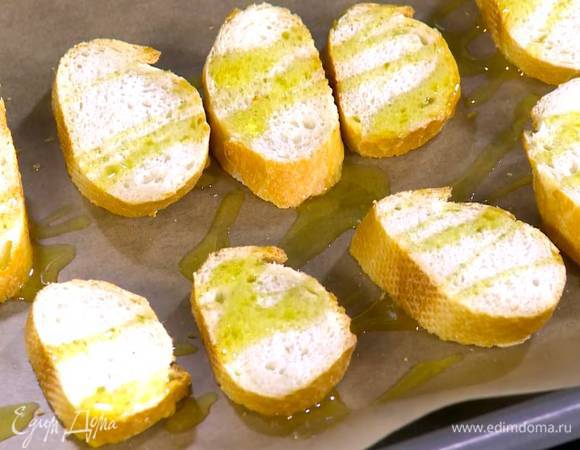 Кусочки хлеба выложить на противень, выстеленный бумагой для выпечки, сбрызнуть 1‒2 ст. ложками оливкового масла Extra Virgin и отправить под разогретый гриль на 1‒2 минуты.