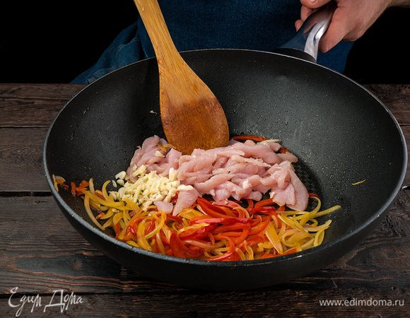 На сковороде обжариваем на растительном масле лук, чеснок и куриное филе, нарезанное на кубики. Добавляем мелко нарезанный болгарский перец, накрываем крышкой на 5 — 7 минут.