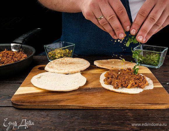 Готовые лепешки выложить на противень, сверху добавить мясную начинку. Разложить зелень и фисташки.
