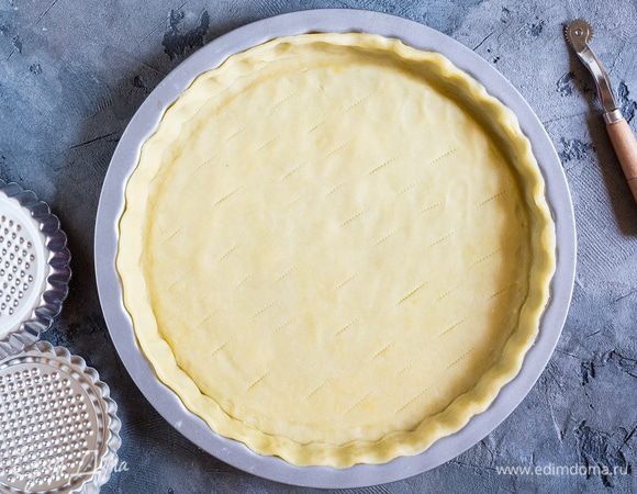 Форму диаметром 24 см смажьте сливочным маслом. Посыпьте мукой рабочую поверхность и скалку и раскатайте тесто до толщины 0,5 см, подсыпая муку по мере необходимости. Неплотно накрутите тесто на скалку, и выстелите им дно и бортики формы. Обрежьте лишнее. Наколите дно вилкой и поставьте в морозилку на 20 минут.