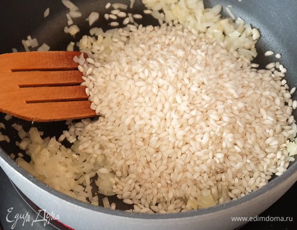 В глубокой сковороде разогреваем немного растительного масла (здесь идеально подойдет виноградное масло Biolio) и обжариваем лук до прозрачности минут 5. Следом добавляем чеснок и засыпаем рис. Рис должен быть сухим!
Жарим смесь 30 секунд, помешивая. Зерна риса должны полностью покрыться маслом и чуть потемнеть снаружи.