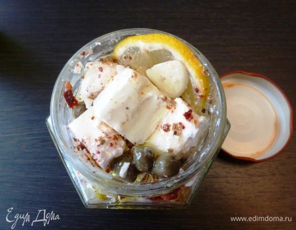 Кубиками брынзы заполнить банку, пересыпая слайсами чеснока, колечками лимона, чили, каперсами и измельченными специями. Залить лимонным соком и ароматным маслом. Оставить в холодильнике на 12 — 24 часа мариноваться.