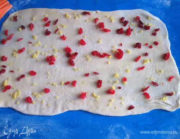 Слегка присыпать сахарным песком, измельченной цедрой лимона, вяленой клюквой и  вишней, которые следует предварительно нарезать на кусочки. Положить на него второй кусок теста, его так же смазать и присыпать, как и первый. 