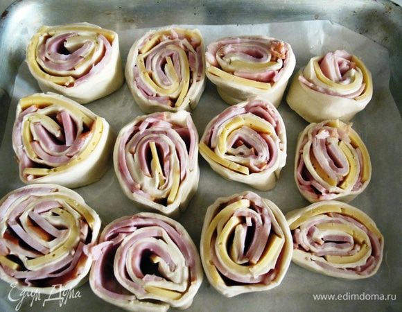 Пласт теста свернуть и нарезать рулетиками. Рулетики выложить на противень.