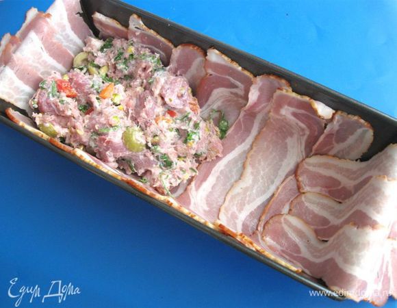 Духовку разогреть до 190°С. Прямоугольную форму слегка смазать  оливковым маслом, выстелить пластинками бекона так, чтобы одна пластина немного заходила на другую. Выложить начинку. 