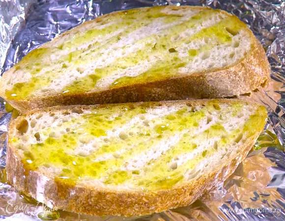 Хлеб выложить на противень, выстеленный пищевой фольгой, сбрызнуть оливковым маслом и поджаривать пару минут под разогретым грилем.