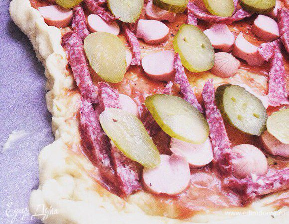 Начинаем готовить начинку, режем все необходимое, смазываем тесто для пиццы соусом (я делала кетчуп + майонез и сверху приправа), затем раскладываем нарезанные колбасу, сосиски, огурцы.