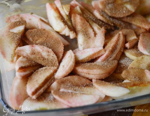 Форму для выпечки смазываем сливочным маслом, выкладываем в нее нарезанные яблоки и присыпаем 2 — 3 ч. л. сахара, корицей и немного перемешиваем.