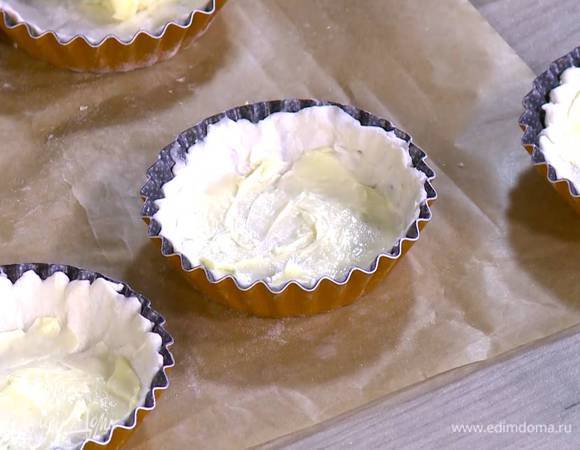 Небольшой формой для тарталеток вырезать из теста круги, уложить их в формочки и равномерно распределить по дну и стенкам, так чтобы получились бортики.