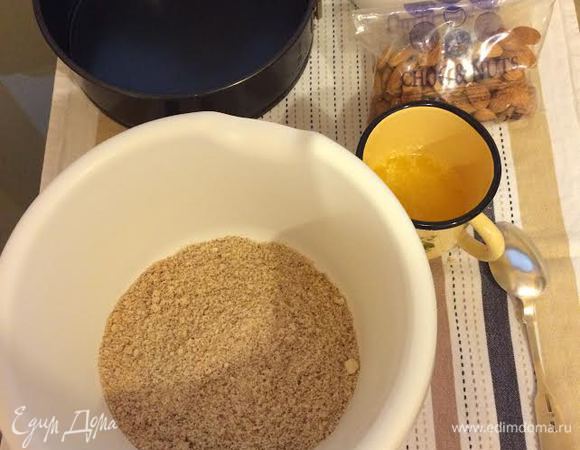 Уменьшить температуру духовки до 170°С. В миске смешать молотое печенье и молотый миндаль. Добавить растопленное сливочное масло.