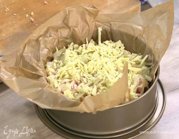 Разъемную форму для выпечки выстелить бумагой для выпечки, равномерно выложить тесто, сверху разложить оставшуюся ветчину, затем слой обжаренного лука и посыпать все оставшимся натертым сыром.