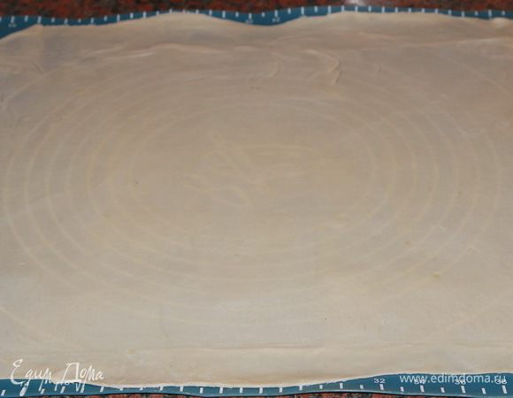 Достаем тесто из холодильника. Далее мы будем готовить пласт вытяжного теста. Поэтому новичкам я рекомендую делать это на присыпанном мукой льняном полотенце. Ну, а я, как уже «матерый» любитель и знаток вытяжного теста, делаю это на силиконовом коврике. А если пласт нужно вытянуть уж совсем-совсем тоненько, например, для пахлавы, то я делаю это на столе. Итак, сначала раскатываем, насколько возможно, наше тесто скалкой. А затем берем его руками и вытягиваем со всех сторон.  Потихоньку, до тех пор, пока тесто не станет настолько тонким, что сквозь него будет видно текстуру того, на чем вы это делаете.