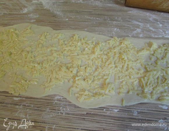 Большой кусочек теста тонко раскатать на припыленной мукой поверхности в прямоугольник. Смазать весь пласт сырно-яичной начинкой (I).