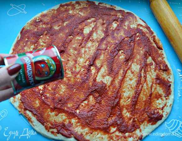 Раскатайте тесто в овал или прямоугольный пласт. Обильно смажьте томатной пастой «Помидорка» и сбрызните оливковым маслом.