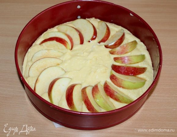 Выложить тесто в смазанную форму, по кругу выложить тонко нарезанные дольки яблок.