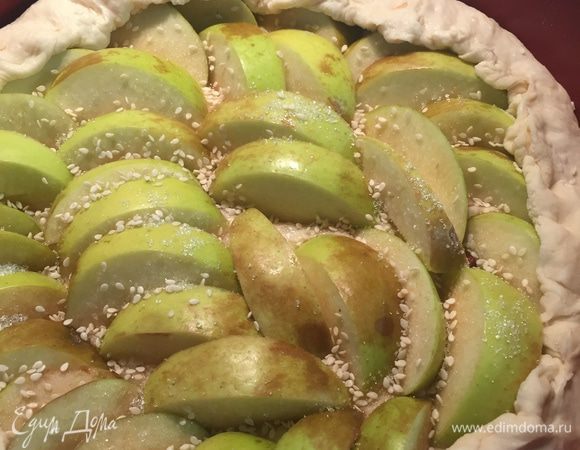 Уложите яблоки на тесто, заверните края, посыпьте сахаром и кунжутом.