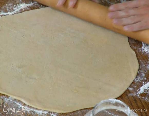 Подошедшее тесто разделить на две части, каждую вымесить руками на посыпанной оставшейся мукой рабочей поверхности, а затем раскатать скалкой в тонкий круг.