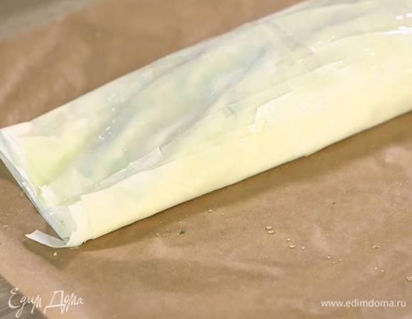 На один край теста выложить начинку и свернуть все в рулет, затем вместе с бумагой перенести на противень и смазать со всех сторон оставшимся оливковым маслом.