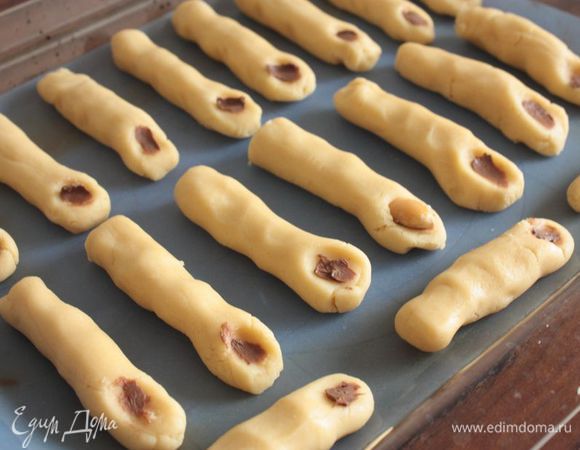 Через полчаса достаньте тесто из холодильника и начинайте лепить пальцы :) Лучше всего скатать тесто в колбаску по толщине пальца, а потом колбаску нарезать на части. Покатайте колбаску между руку, чтобы она стала округлой со всех сторон. 

Когда будете выкладывать печенье на противень, не забудьте немного сплюснуть его по бокам в 2 — 3 местах, чтобы получились фаланги.

Растопите шоколад. Миндаль залейте кипятком и оставьте на пару минут, а затем очистите его. На конце каждого печенье сделайте углубление, смажьте его шоколадом, а сверху уложите миндаль (он играет роль ногтя, а шоколад роль грязи).