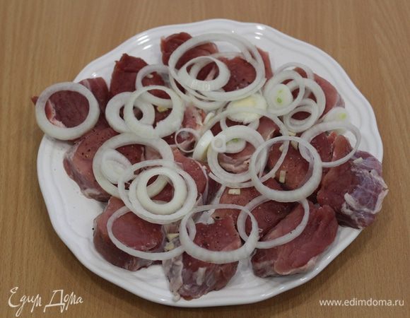 Свинину нарезать небольшими кусочками, слегка отбить. Чеснок мелко нарезать, лук нарезать кольцами. Сложить все на тарелку, посолить, поперчить. Закрыть крышкой и убрать в прохладное место на 1 час.