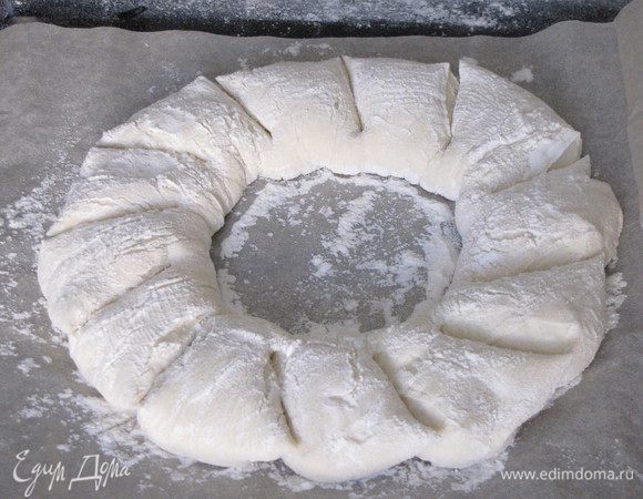 Противень выстелить бумагой для выпечки, положить кольцо. Присыпать мукой. С помощью острых ножниц сделать косые надрезы под углом 45° почти до конца.